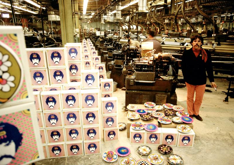 Peter Max in a factory next to a pile of his art clocks