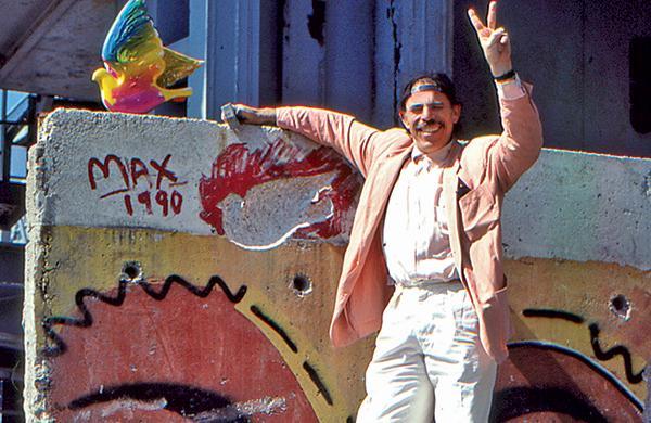 Peter Max holding up peace sign in front of Berlin Wall