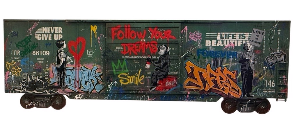 Mr. Brainwash Train Panel: a green freight-car form covered with colorful graffiti, stenciled figures, and painted slogans.