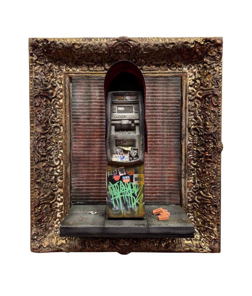 Danny Cortes ATM: graffiti-covered miniature ATM against a brick wall inside an ornate gold-toned frame.