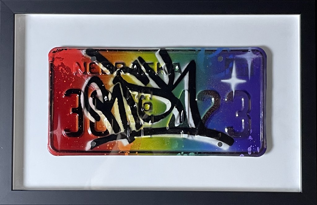 RISK, Risky Plates: rainbow-painted license plate with bold black-and-white graffiti-style marks and white starbursts in a black frame.