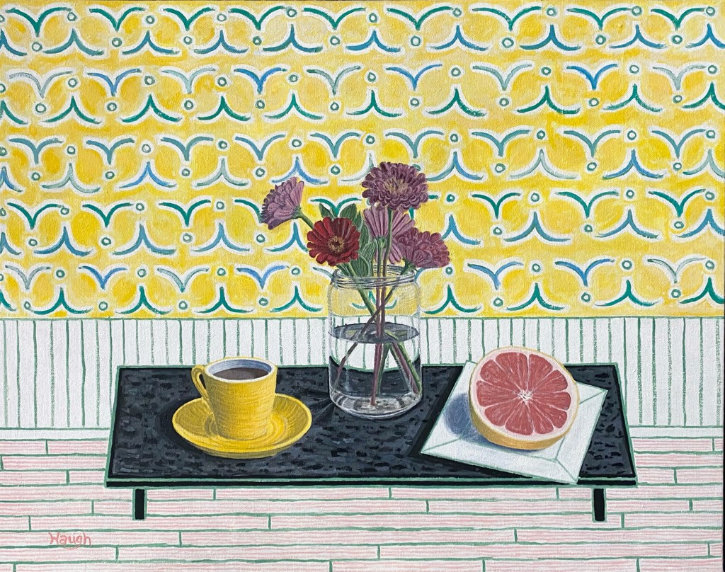 A cup of coffee in a yellow mug on a saucer, a 1/2 sliced grapefruit and a vase of red crysanthimums sit on a black rectangular table with short legs against a simple background of wooden floor boards at the base, vertical lines across just above, and yellow wallpaper with a blue pattern.