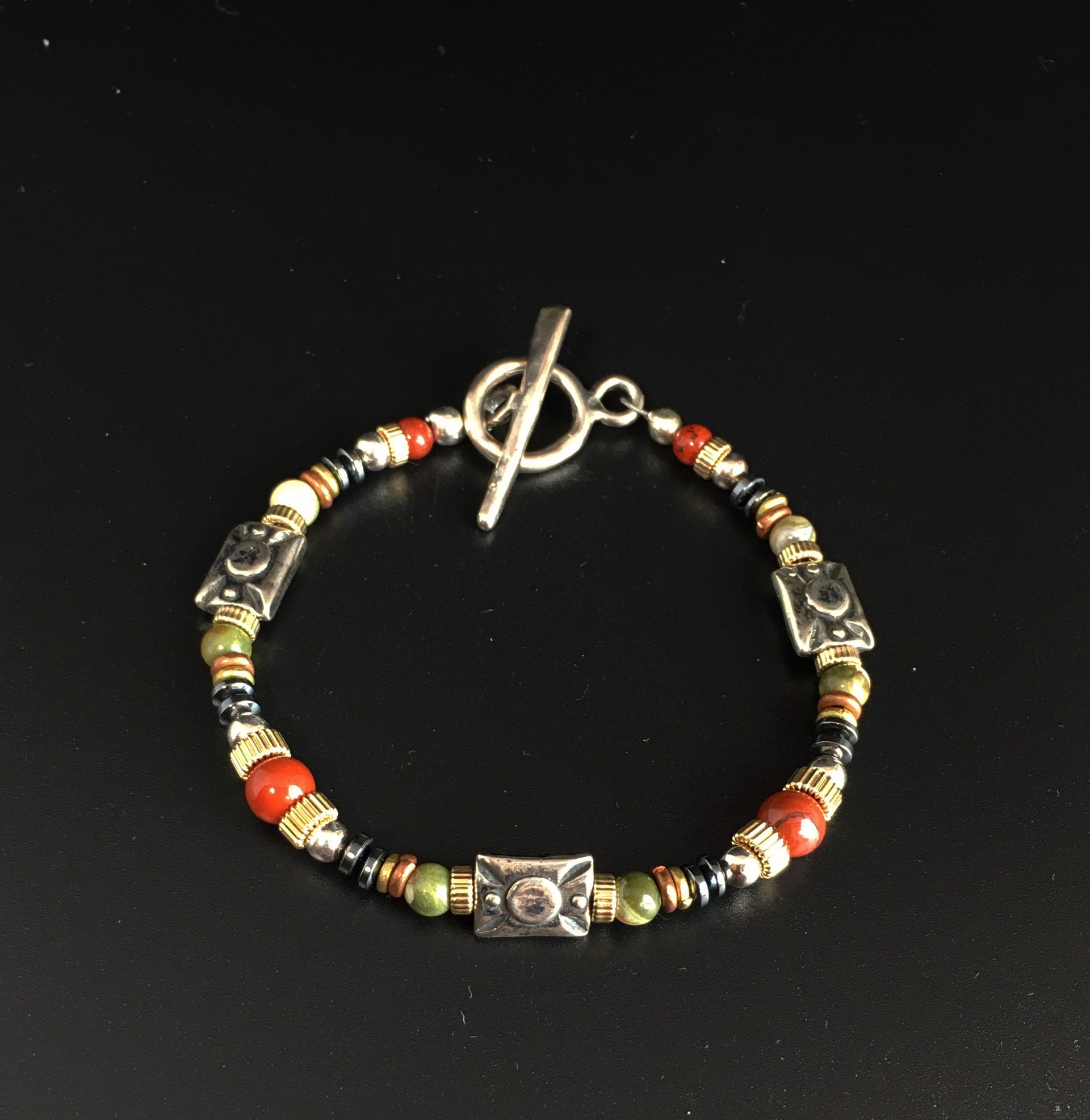 These earth tones are warm and colorful yet go with everything! They feature Sarah's own designer ancient bronze or sterling silver pieces, copper, 14k gold fill, poppy jasper, rhyolite and hematite. The designer beads measure roughly 3/8” and are a bit m by Sarah Foster