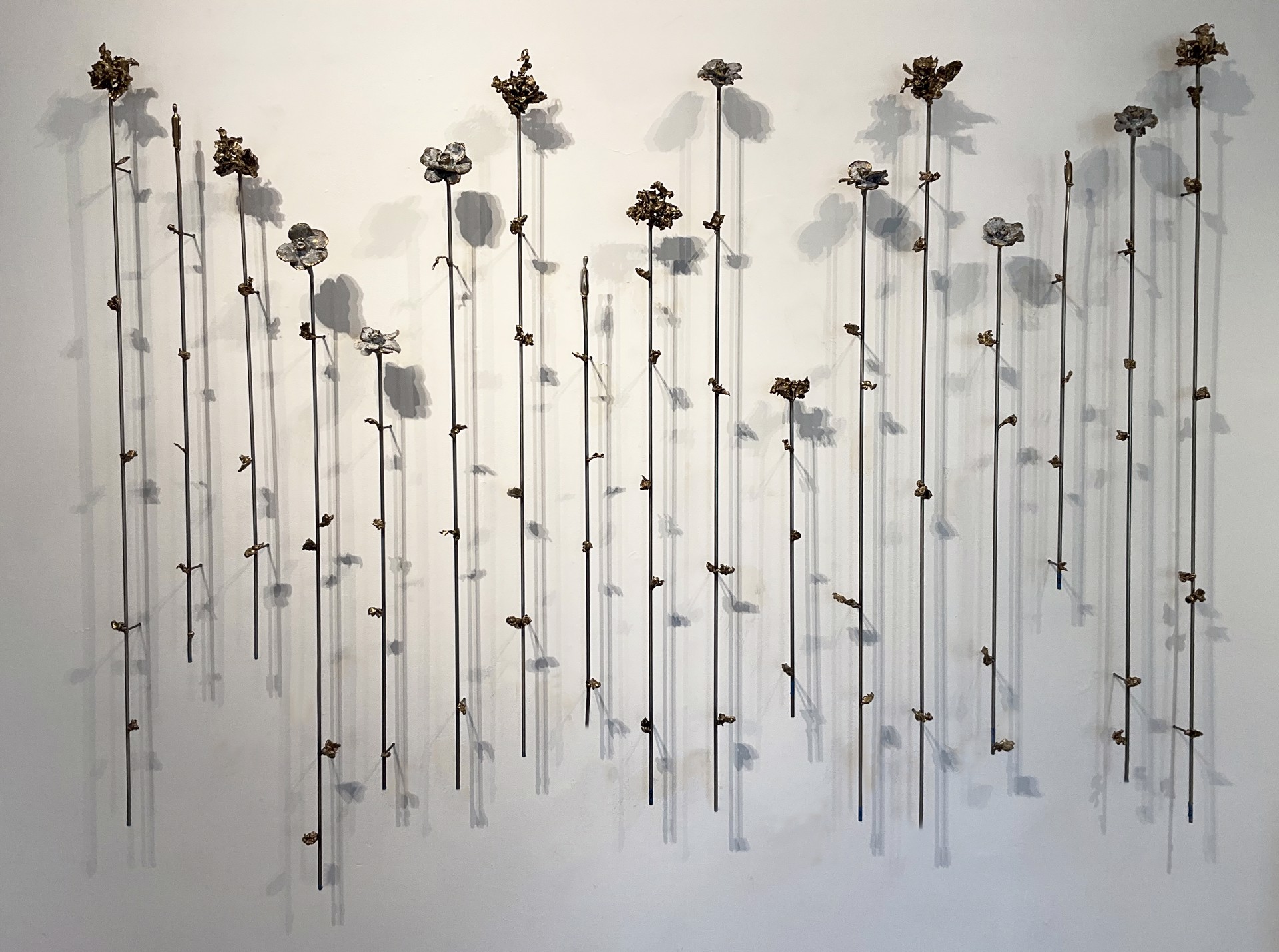 A wall sculpture of individually mounted bronze and steel flowers and figures