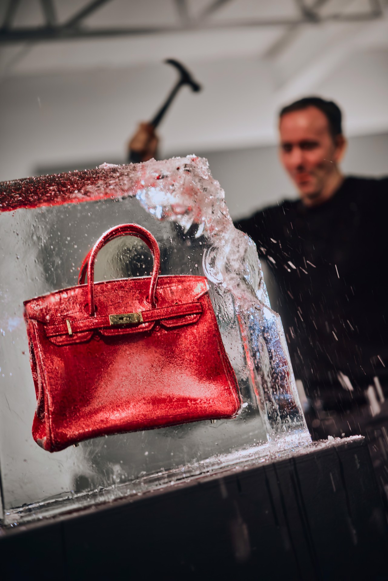Tyler Shields striking the block of ice holding a red Birkin at Samuel Lynne Galleries