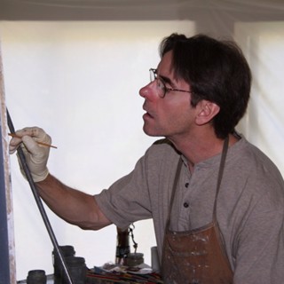Fine artist Daniel Sprick intently focused on his work, painting with precision in his studio. Wearing glasses and a painter’s apron, he holds a thin brush delicately, his hand steady with the assistance of a mahlstick for support. His concentrated expression reflects his meticulous approach to realism, capturing fine details with patience and skill. The soft, neutral lighting in the studio highlights his careful technique and dedication to craft, embodying the disciplined artistry that characterizes Sprick’s detailed portraits and still life paintings. Fine artist Daniel Sprick intently focused on his work, painting with precision in his studio. Wearing glasses and a painter’s apron, he holds a thin brush delicately, his hand steady with the assistance of a mahlstick for support. His concentrated expression reflects his meticulous approach to realism, capturing fine details with patience and skill. The soft, neutral lighting in the studio highlights his careful technique and dedication to craft, embodying the disciplined artistry that characterizes Sprick’s detailed portraits and still life paintings.
