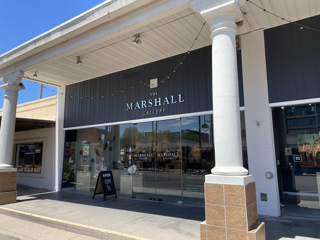 The image shows the storefront of Marshall Outfitters with a modern black and glass design in a shopping plaza.